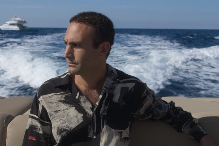 TheCrown_Season6_FirstLook1 Khalid Abdalla as Dodi Fayed in The Crown season 6 sat aboard a yacht staring to the left of the frame.